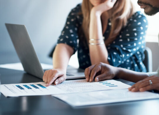 Cropped shot of a businessman and businesswoman using a laptop while going through paperwork together in a modern office