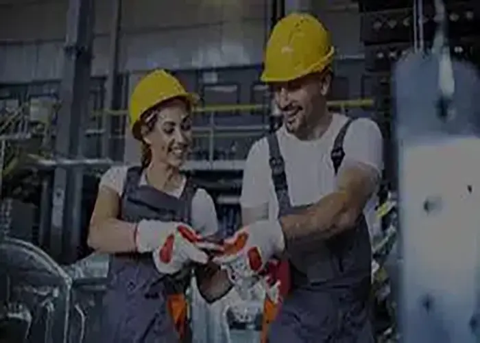 Two field service professionals wearing yellow hard hats, safety gloves, and work uniforms collaborate in an industrial facility, representing Ambit Software’s launch of Field Service Management for SugarCRM.