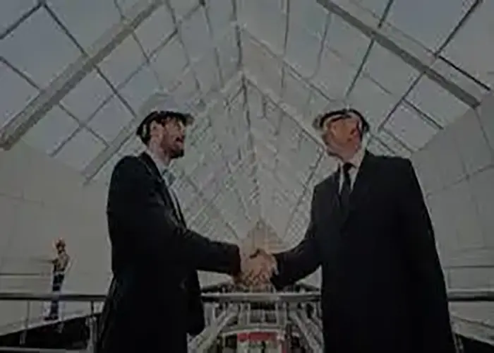 Two business professionals shaking hands in a modern industrial facility, symbolizing a partnership in field service management.
